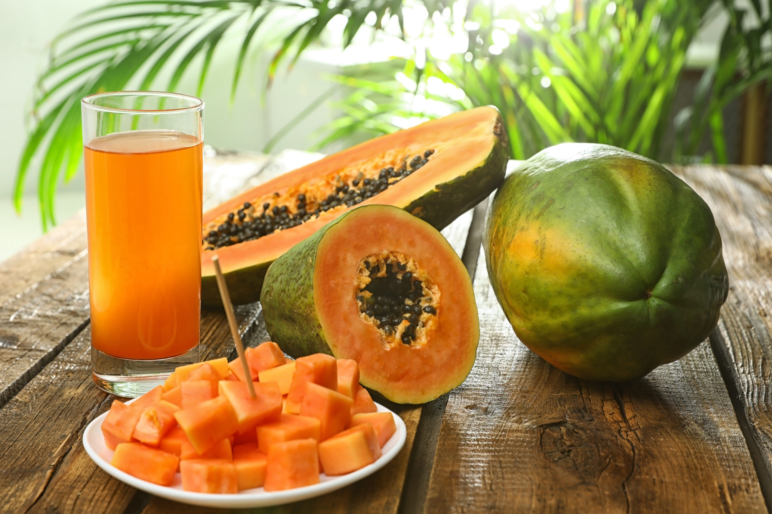 Fresh papayas and juice on wooden table against blurred background